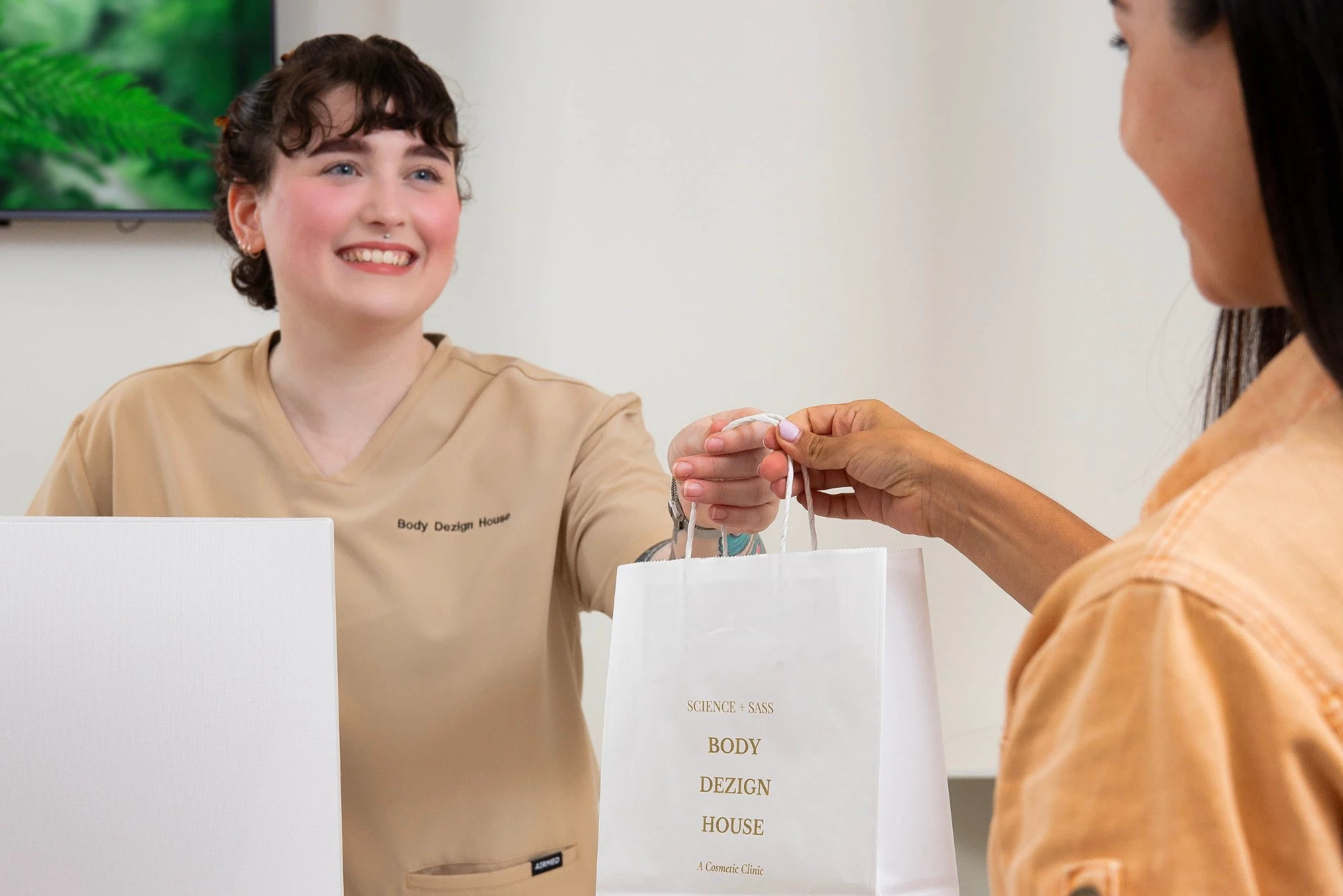 A Body Dezign House team member handing a branded gift bag to a client at the Newstead, Brisbane clinic